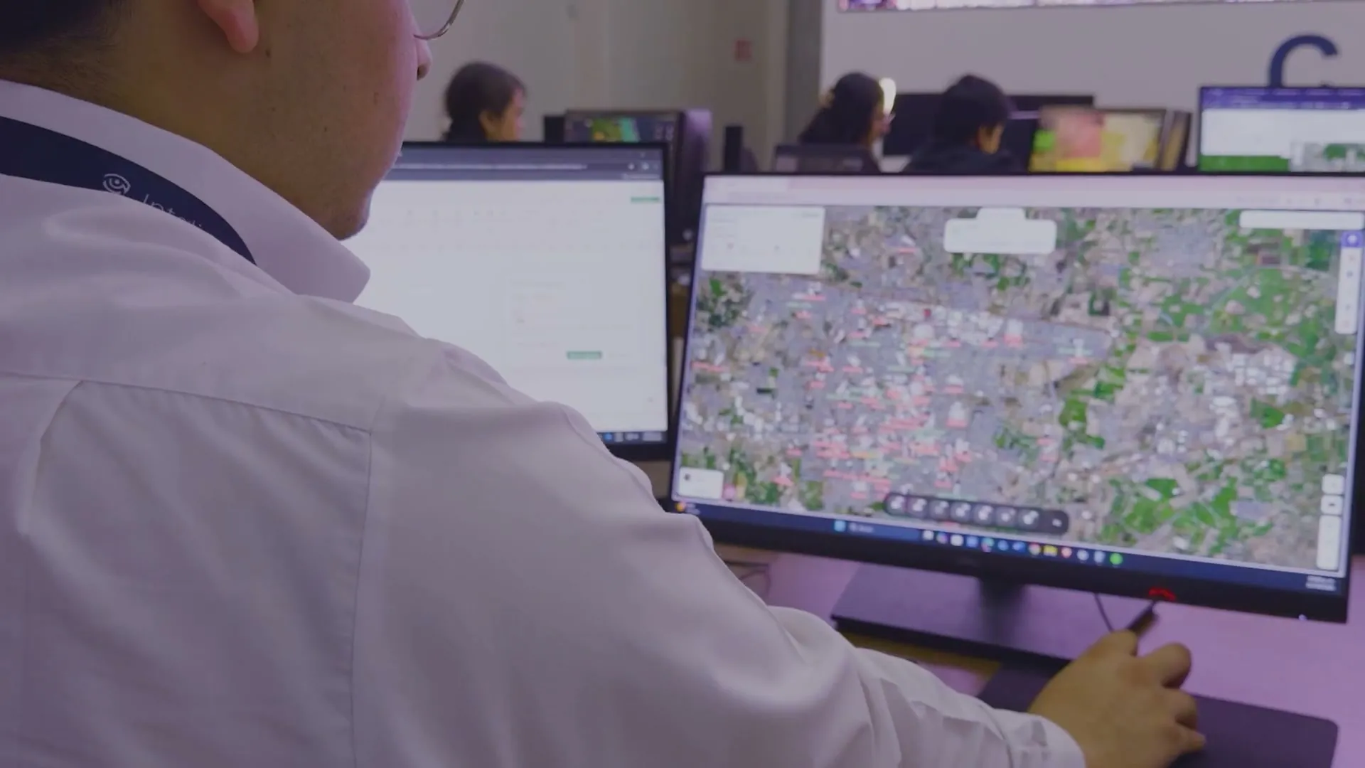 Un operador frente a sus monitores en el centro de monitoreo, con compañeros trabajando al fondo.